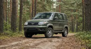 A dark green five-door SUV is parked on a dirt track surrounded by a dense forest of tall pine trees. It has a winged